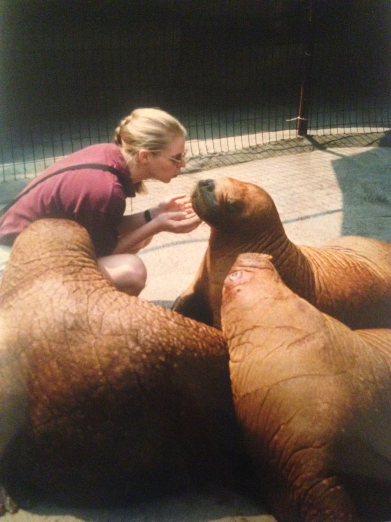 A young Jen crouching down and surrounded by three baby walruses.